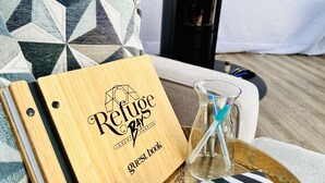 Un libro de visitas de madera con la inscripción "Refuge Bay Luxury Camping", colocado sobre una bandeja junto a un vaso con pajita.