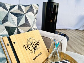 Ein hölzernes Gästebuch mit der Aufschrift "Refuge Bay Luxury Camping", platziert auf einer Ablage neben einem Glas mit Trinkhalm.