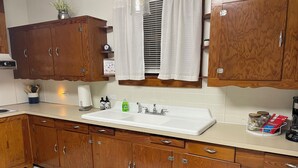 A kitchen with wooden cabinets, a white sink, and a window with white curtains.
