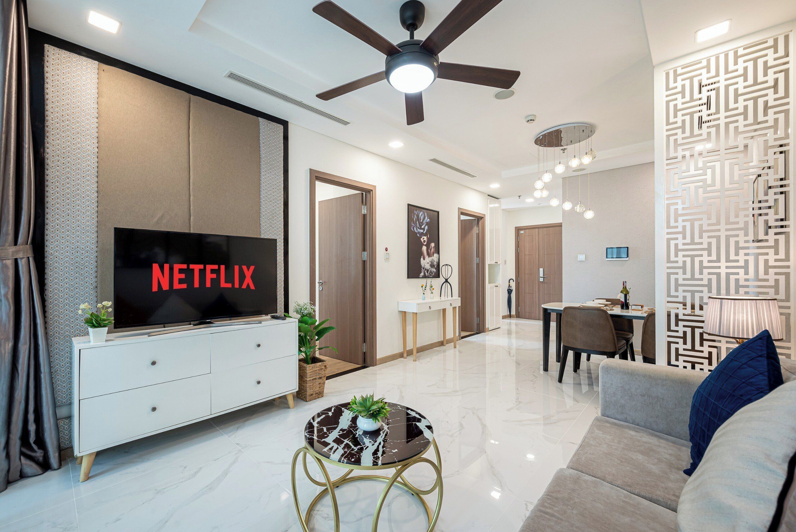 A modern living room with a flat-screen TV, a ceiling fan, a dining area, and a patterned wall.
