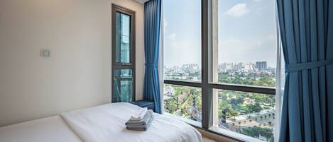 Habitación de hotel moderna con un ventanal grande que ofrece vistas a la ciudad, una cama bien hecha y una pequeña zona de estar.