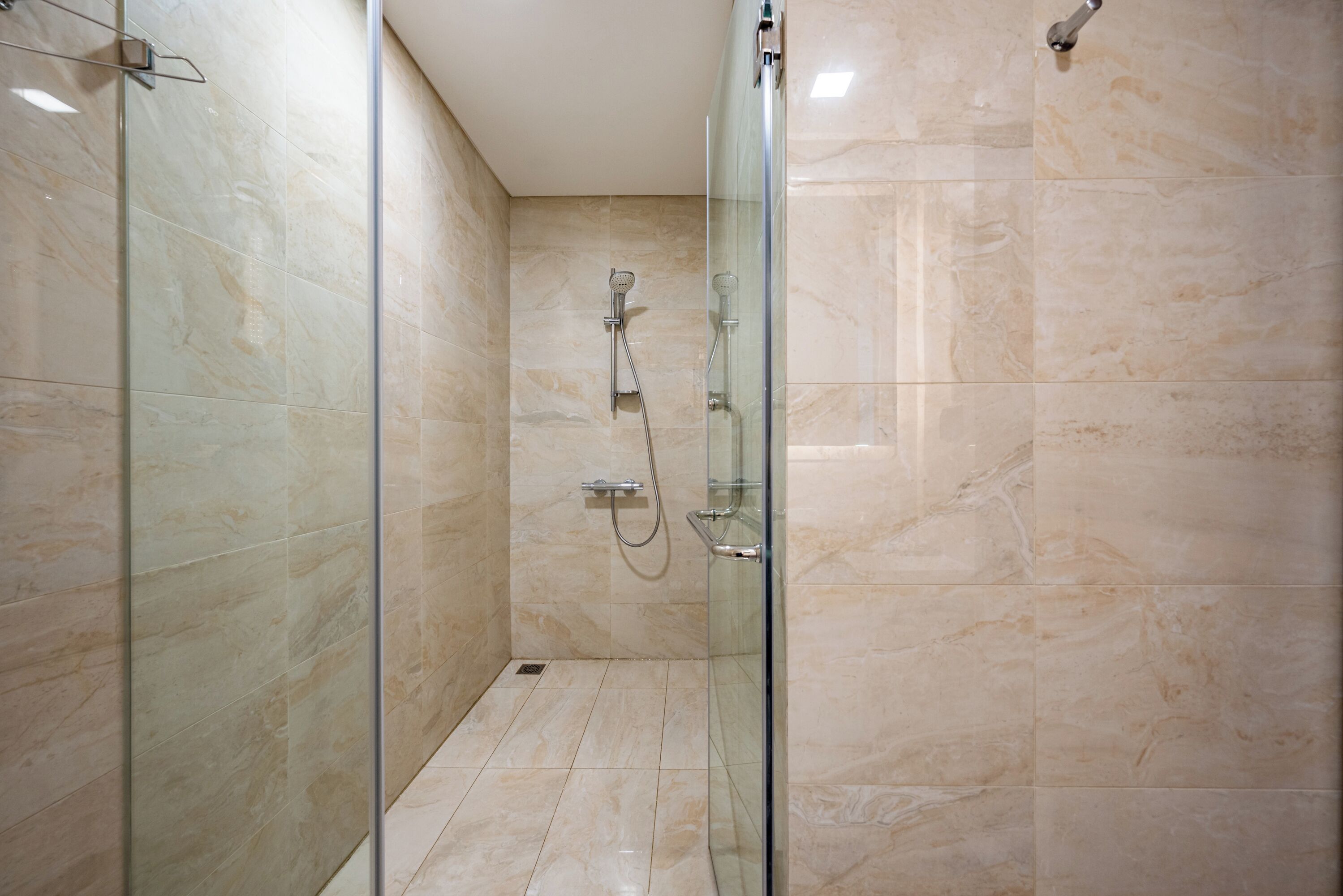 Eine begehbare Dusche mit Glastrennwand, einer Handbrause und einem am Wand montierten Wasserhahn.