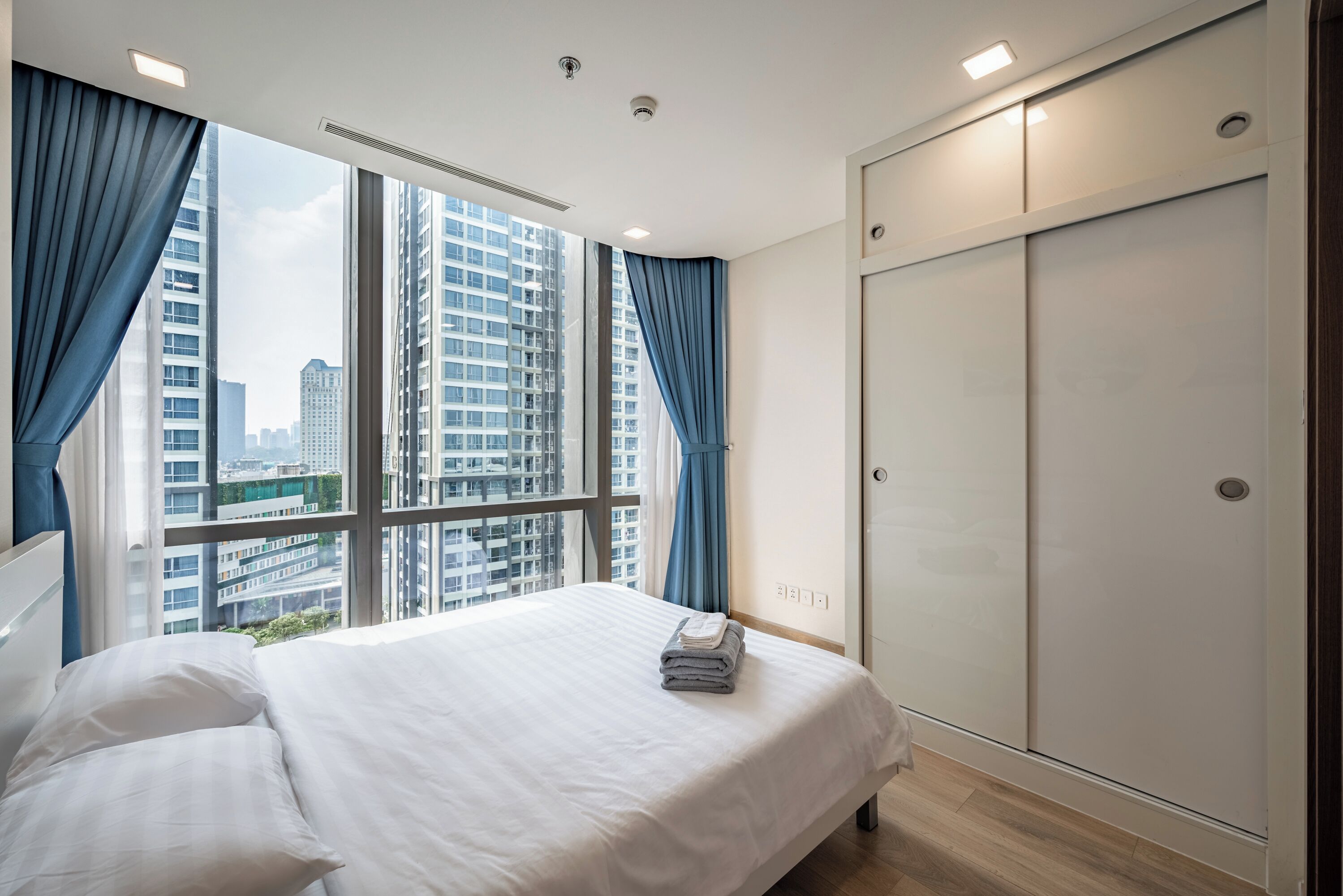 Ein Hotelzimmer mit einem großen Bett, einem Kleiderschrank und Blick auf hohe Gebäude.
