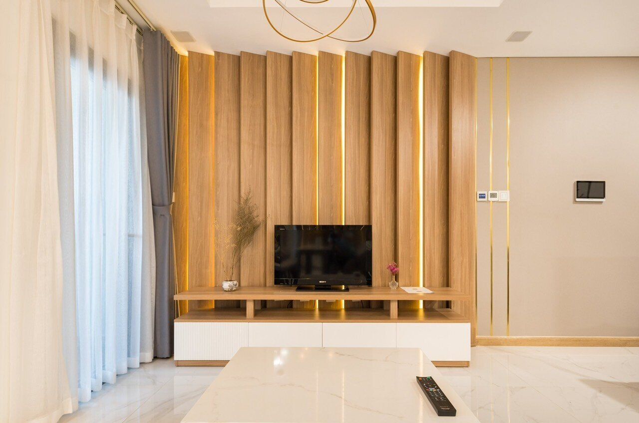 Uma sala de estar moderna com uma TV de tela plana sobre um móvel de madeira, uma mesa de centro de mármore e um controle remoto na mesa.