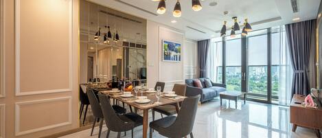 A modern dining area with a large table set for six, surrounded by chairs. A large mirror and a painting are visible on the walls.