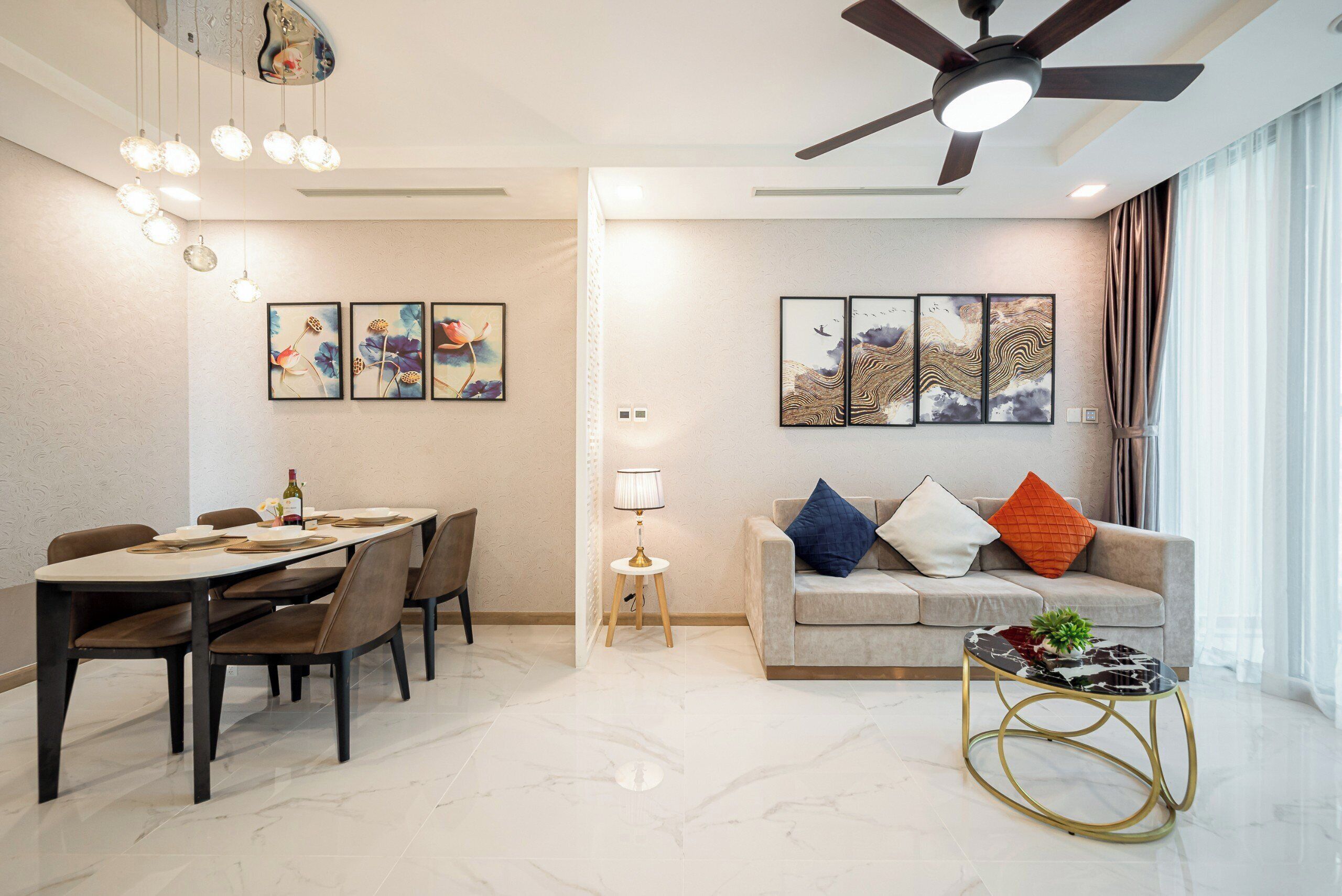 A modern living room with a dining area, featuring a sofa, coffee table, and artwork on the walls.