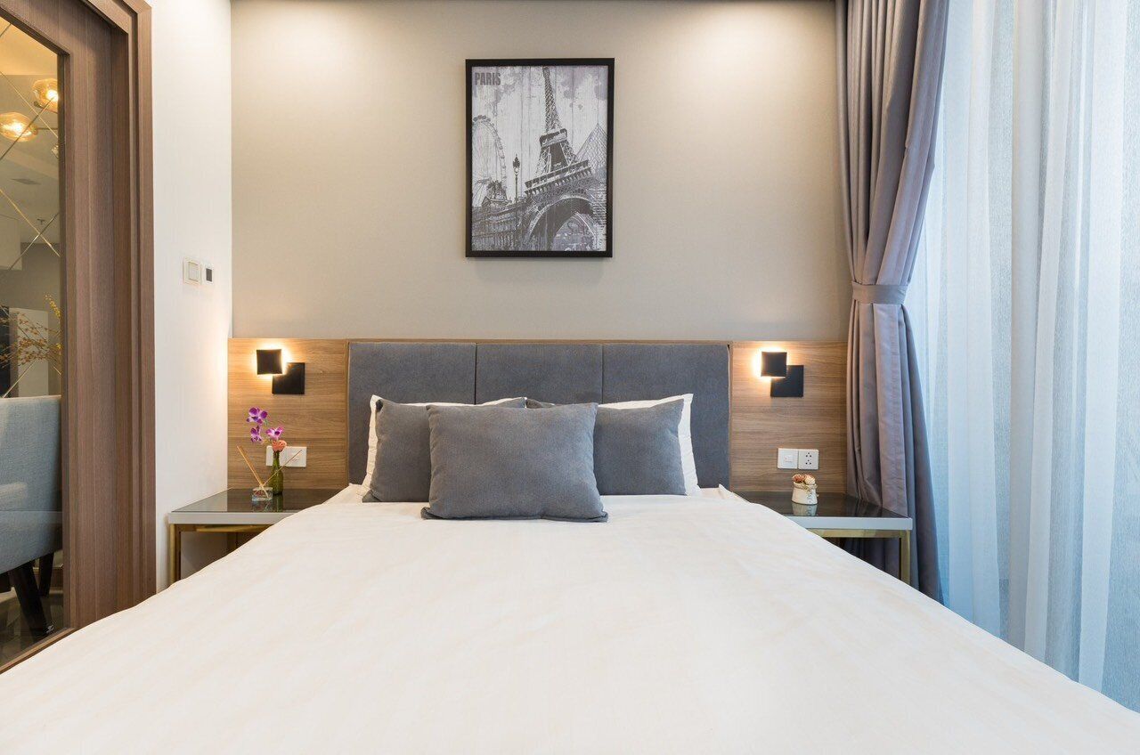 A hotel room with a large bed, two bedside tables, a framed picture on the wall, and a window with curtains.