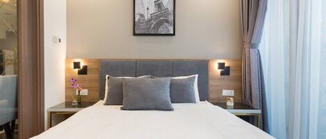 A hotel room with a large bed, two bedside tables, a framed picture on the wall, and a window with curtains.