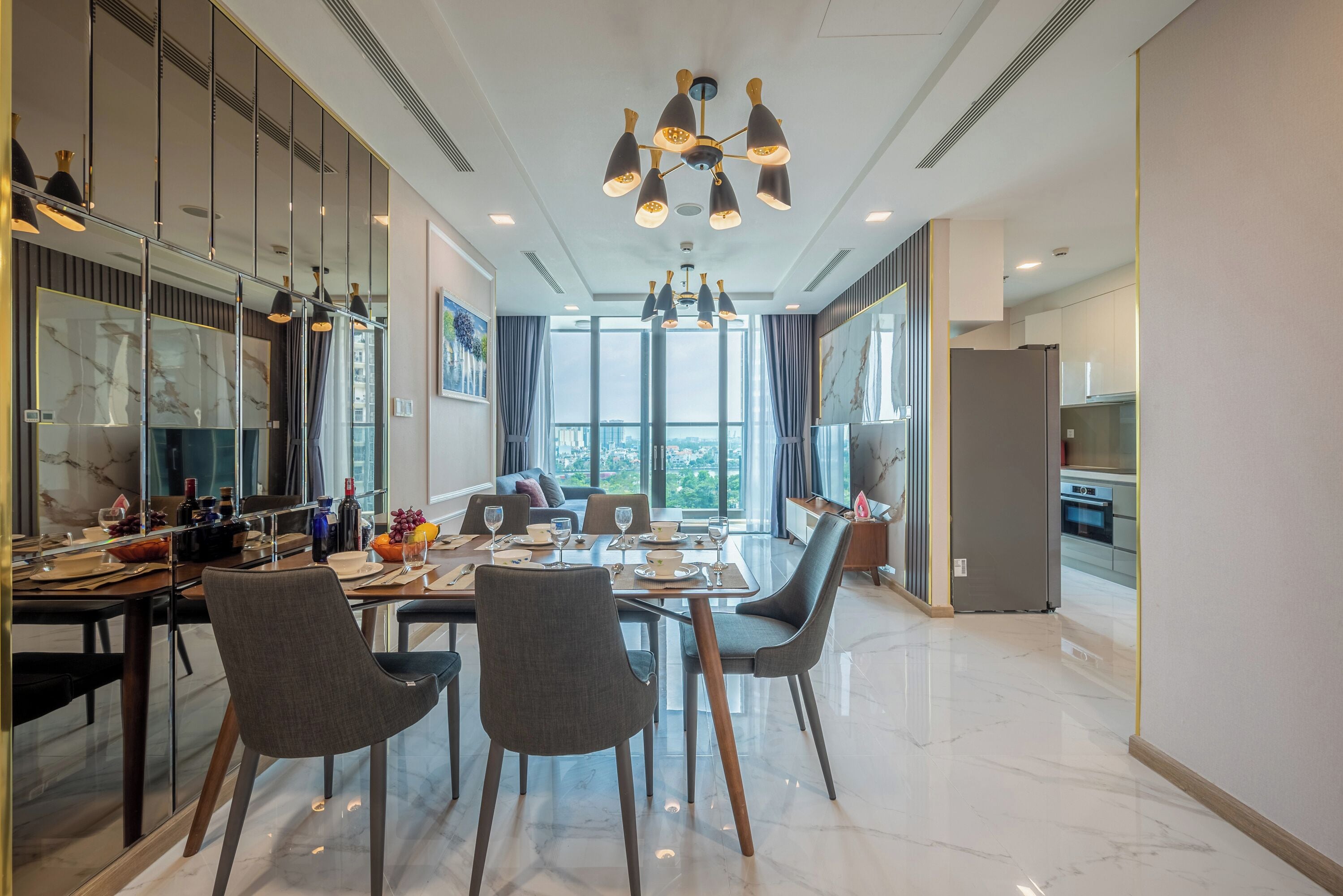 Uma sala de jantar moderna com piso de mármore, uma mesa grande posta para quatro pessoas e um lustre contemporâneo.