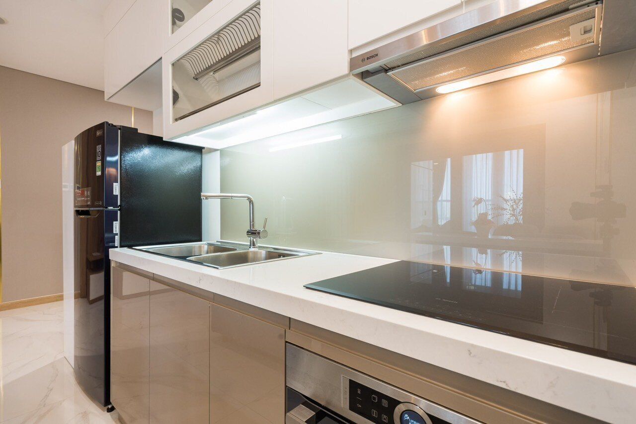 A modern kitchen with a black refrigerator, stainless steel sink, and a built-in oven.