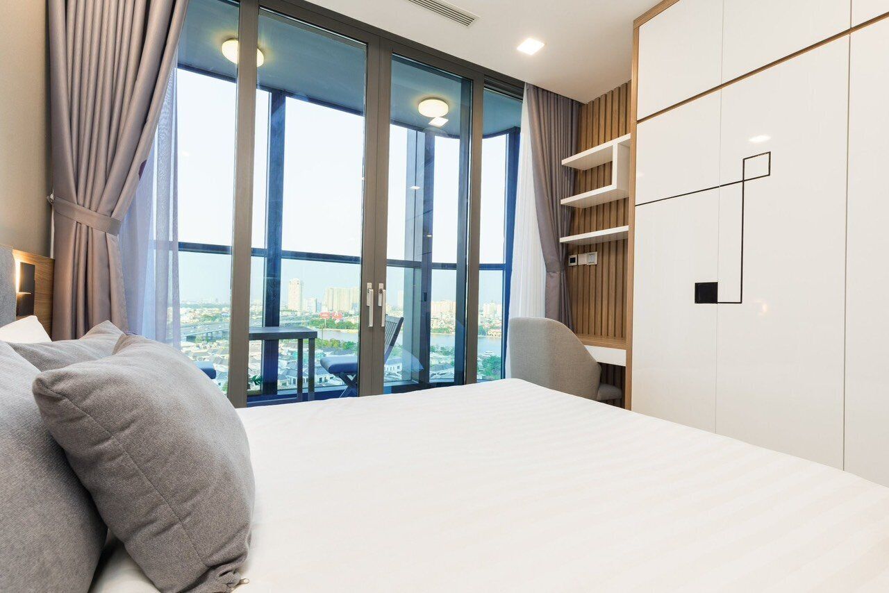 Una habitación de hotel moderna con una cama grande, vistas de la ciudad a través de ventanales y un diseño minimalista.