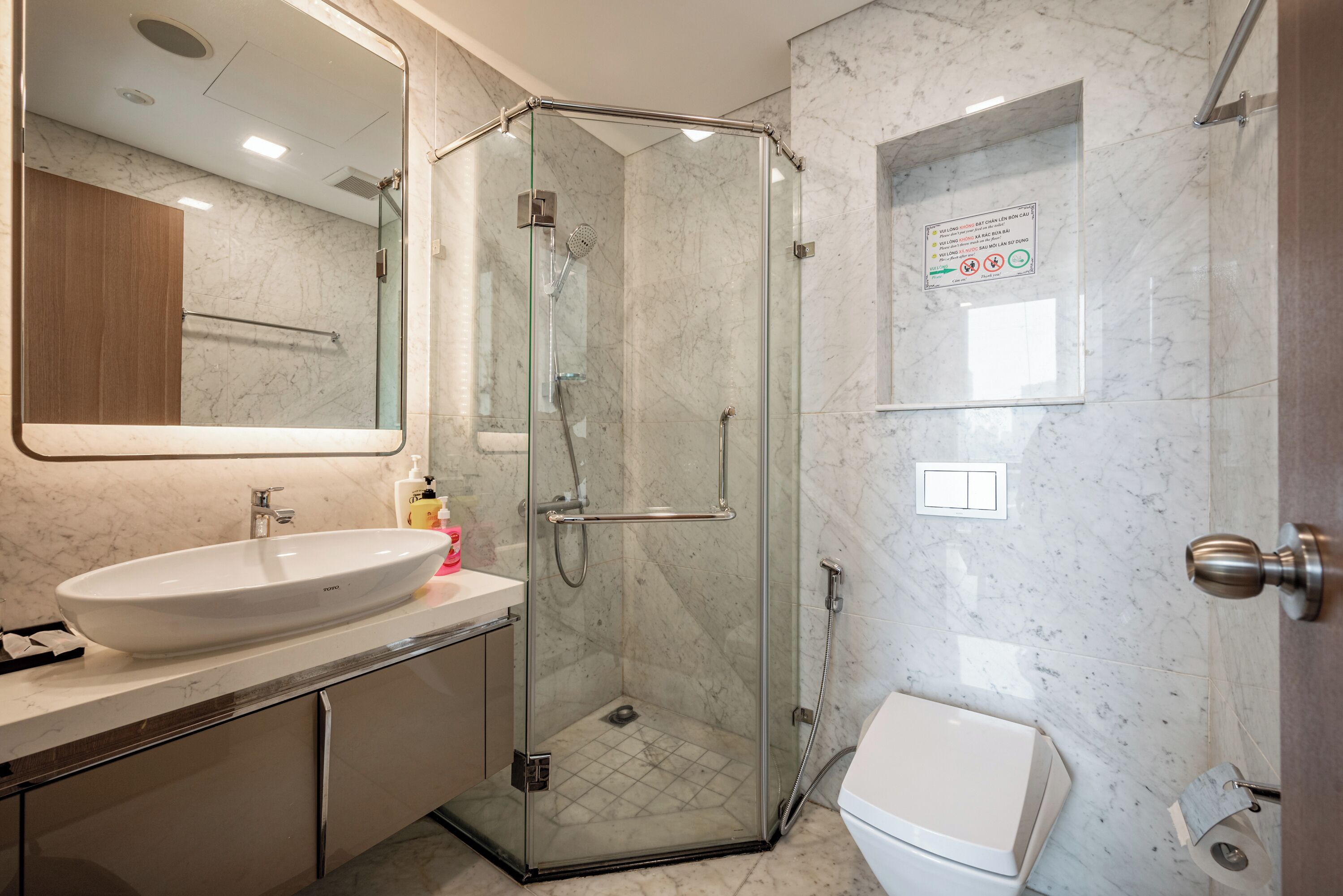 A modern bathroom with a glass-enclosed shower, a white sink, and a toilet.