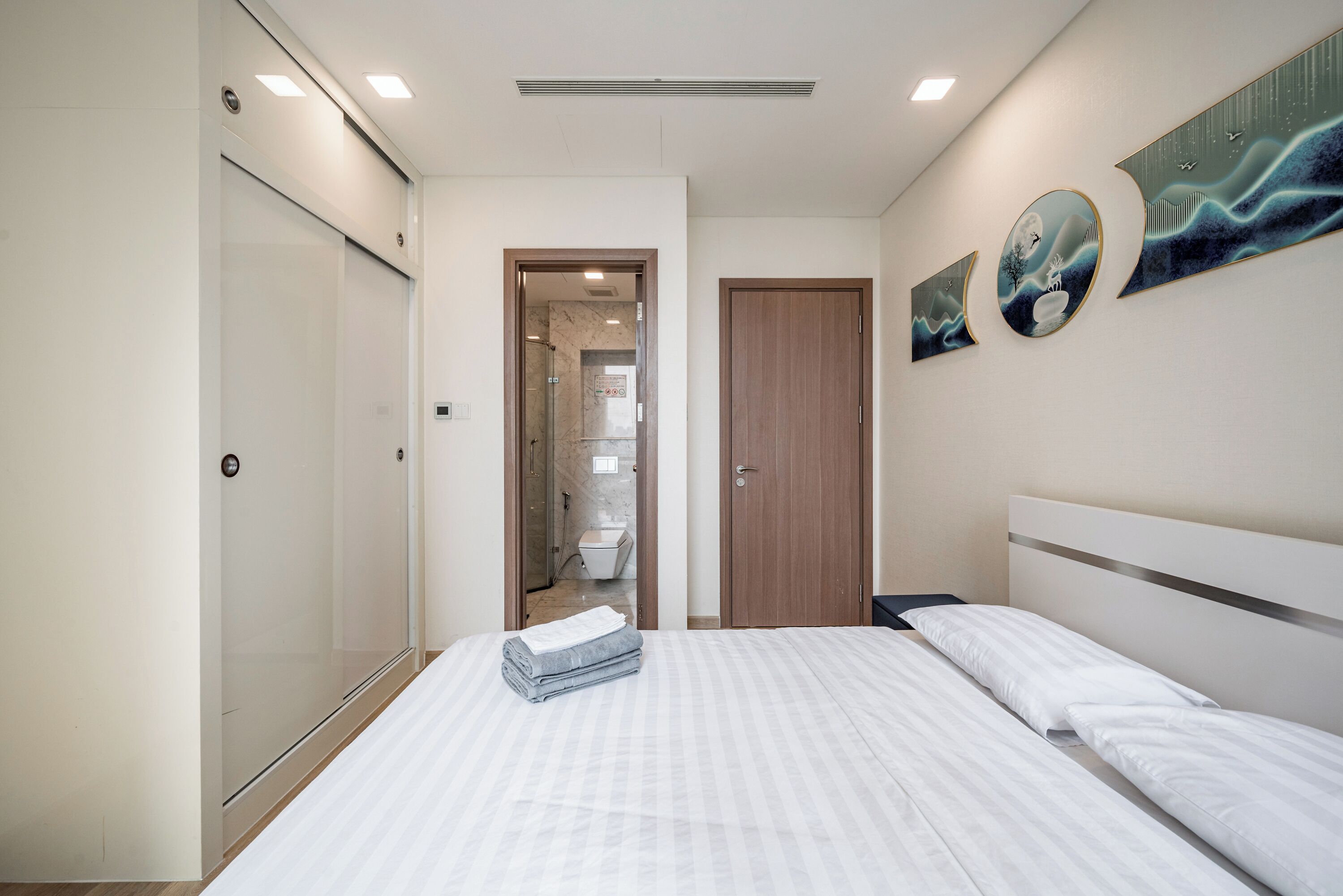 Una camera da letto moderna con un letto grande, una porta in legno e un bagno visibile attraverso una porta aperta.