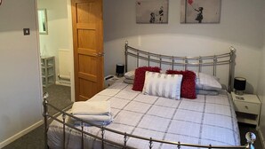 A bedroom with a metal bed frame, a wooden door, a bedside table with a lamp, and two wall-mounted artworks. - 1-Bedroom Apartment Sleeps 4, Parking (Hythe)
