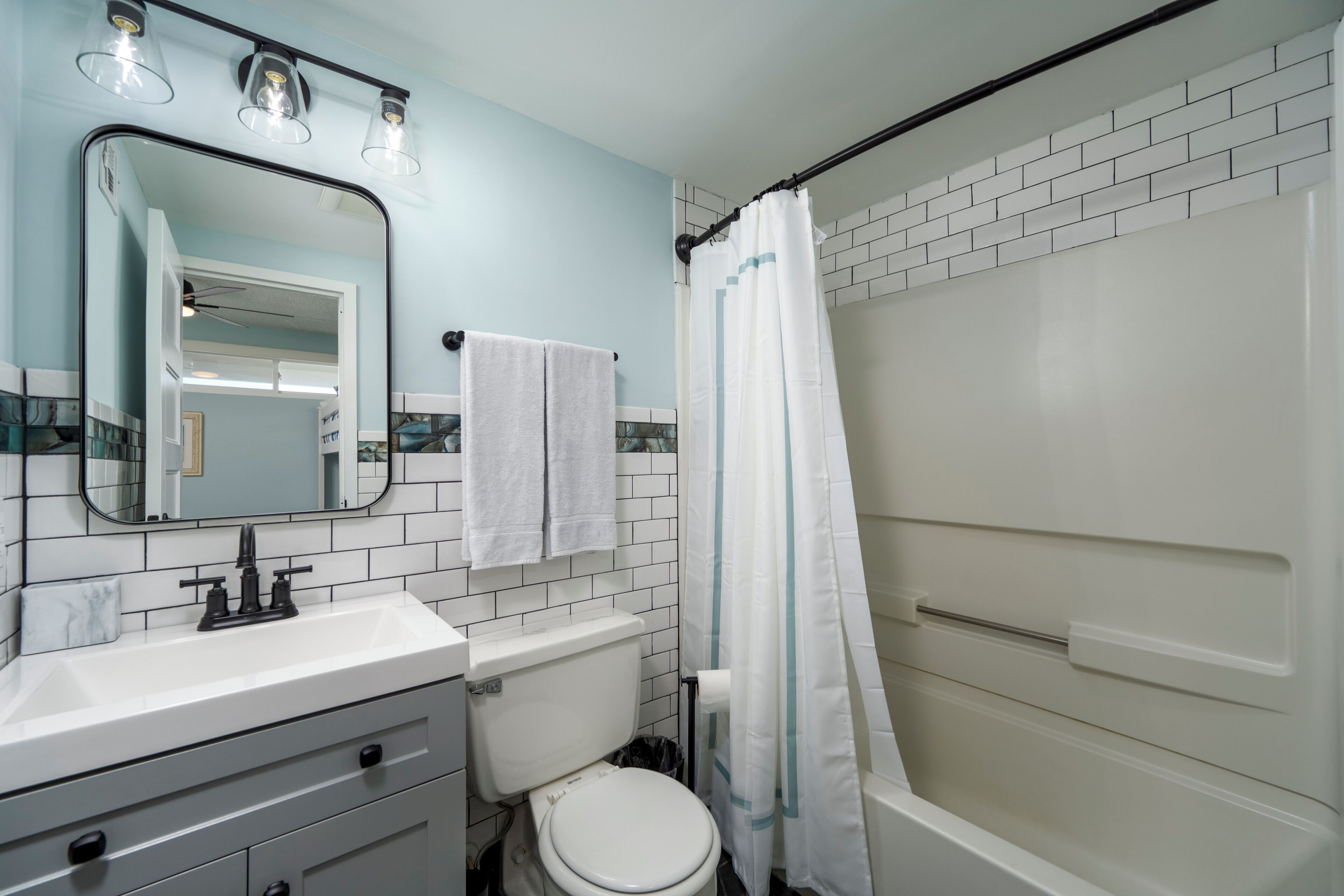 A bathroom with a white sink, mirror, and toilet, a shower with a white curtain, and a light blue wall.
