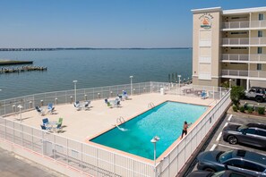 A swimming pool with a view of the water, a dock, and a building with a balcony. - Ocean City Bayside Condo, Newly Renovated (Ocean City)
