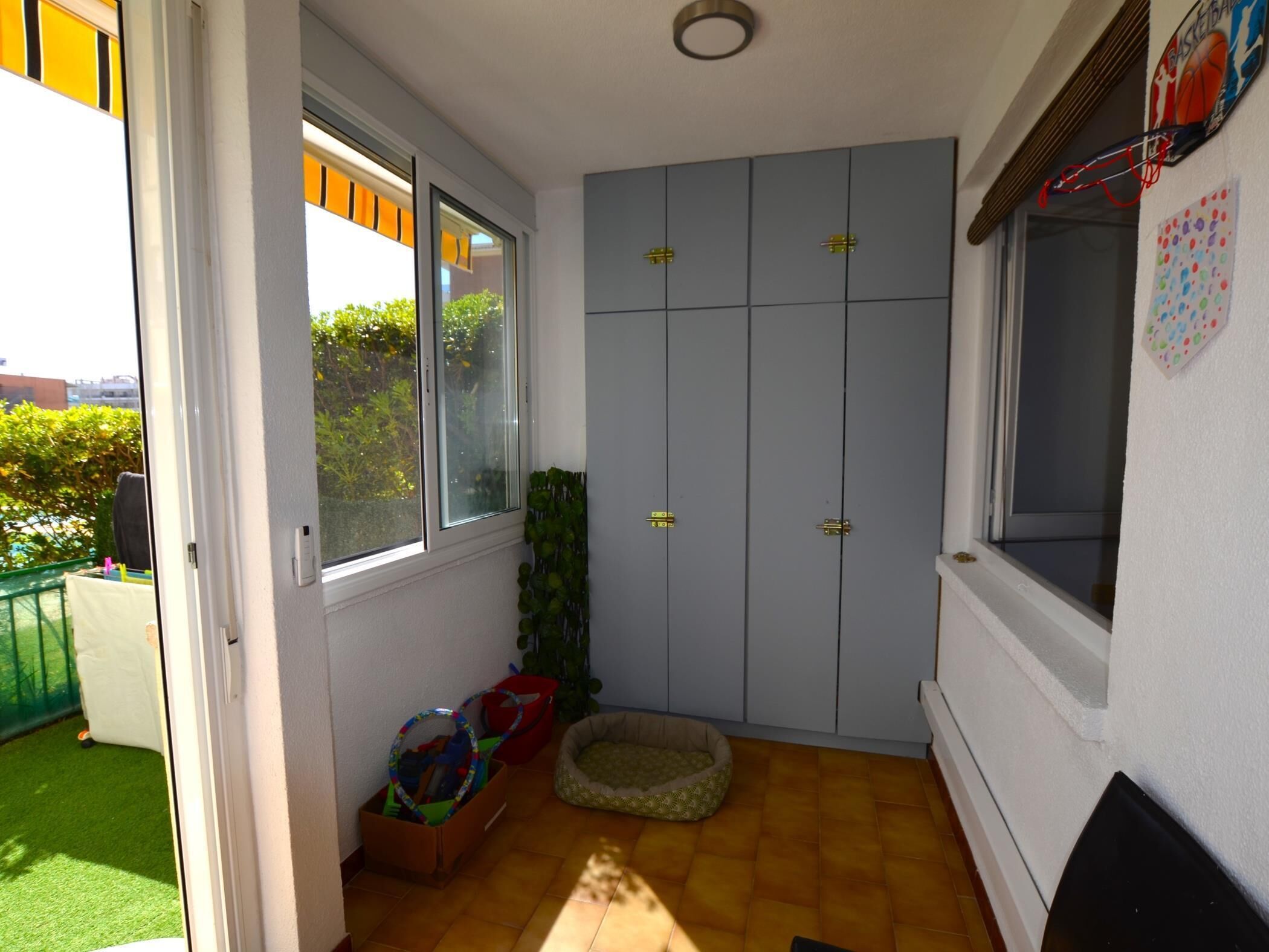 A room with a sliding door leading to a balcony, a pet bed, a storage box, and a basketball hoop on the wall.