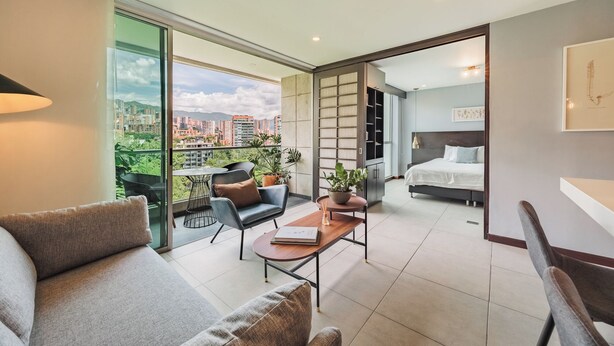 Een modern appartement met balkon, een bank, een eettafel en een slaapkamer met een bed en nachtkastje.