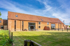 A large brick building with a sloped roof, a large open door, and a fenced outdoor area.