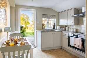 Una cocina con una mesa de comedor lista para el desayuno, una ventana con vista al jardín y un horno empotrado.