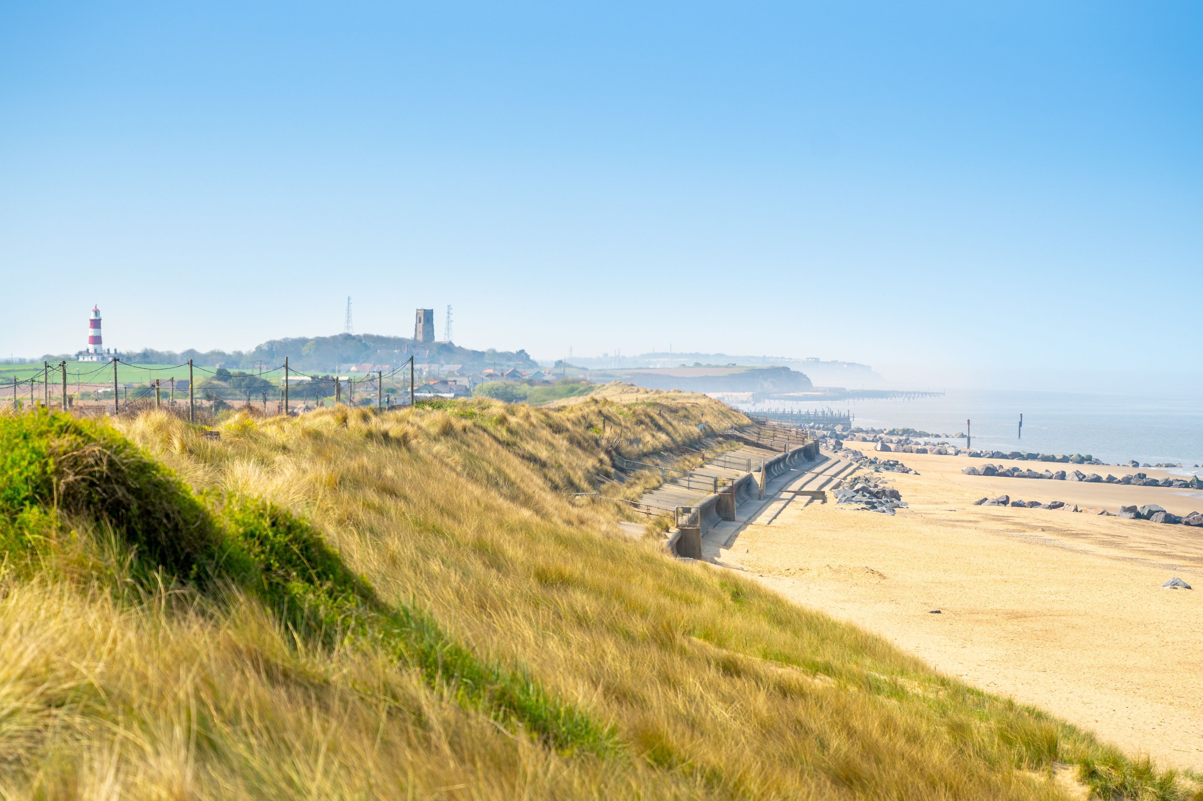 Een kustlandschap met een vuurtoren, een strand en een uitgestrekte stad aan de horizon.