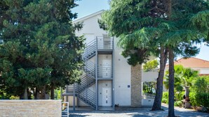 A building with a metal staircase leading to an entrance, surrounded by trees and a paved area. - Picigin by Interhome (Zadar/Bibinje)