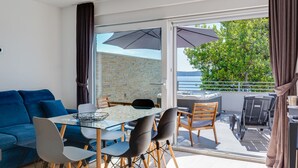 Ein modernes Wohnzimmer mit einem Glastisch, einem blauen Sofa und einem Balkon mit Gartenmöbeln.