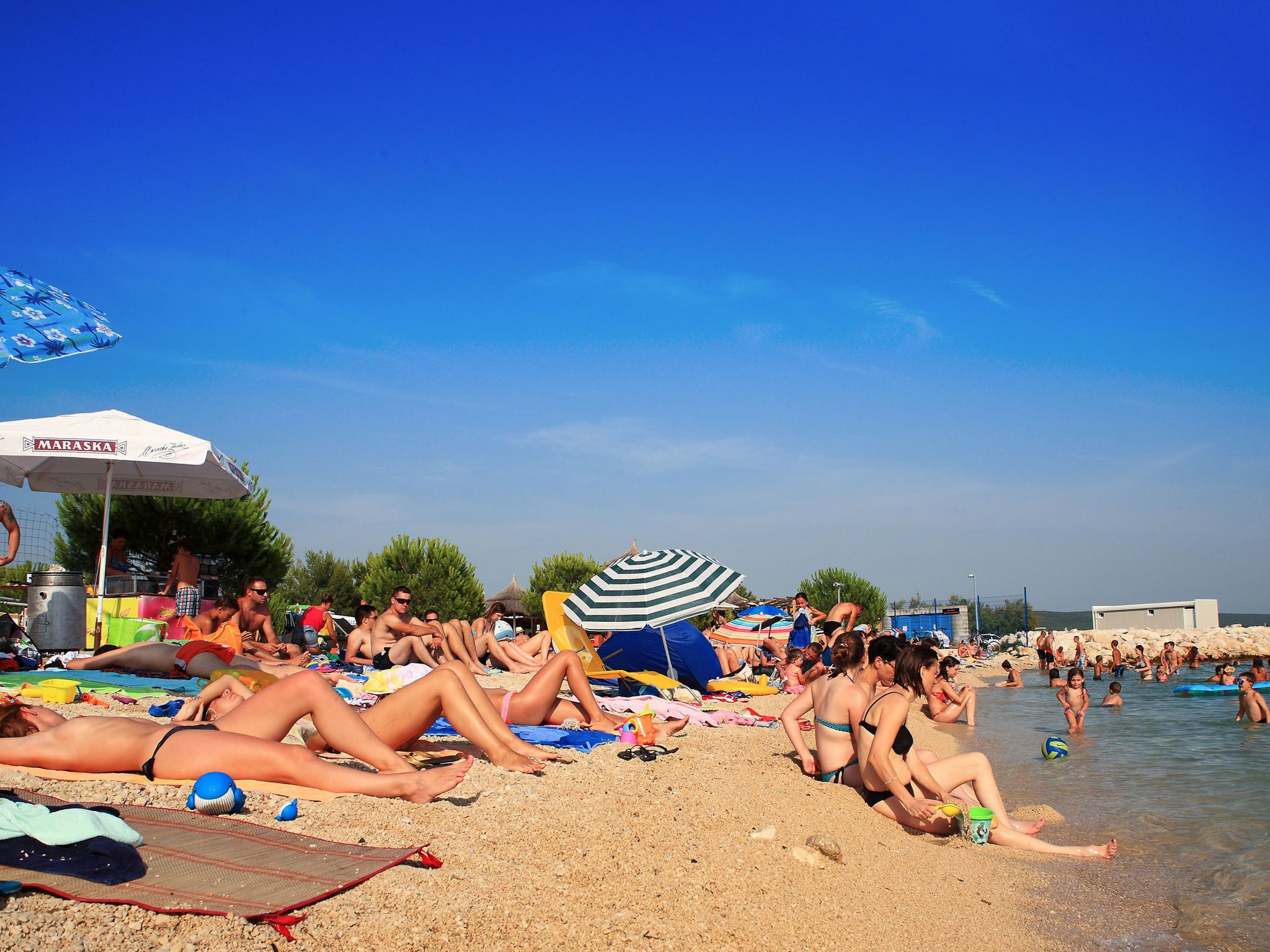 Une plage bondée où les gens se prélassent au soleil et se baignent.