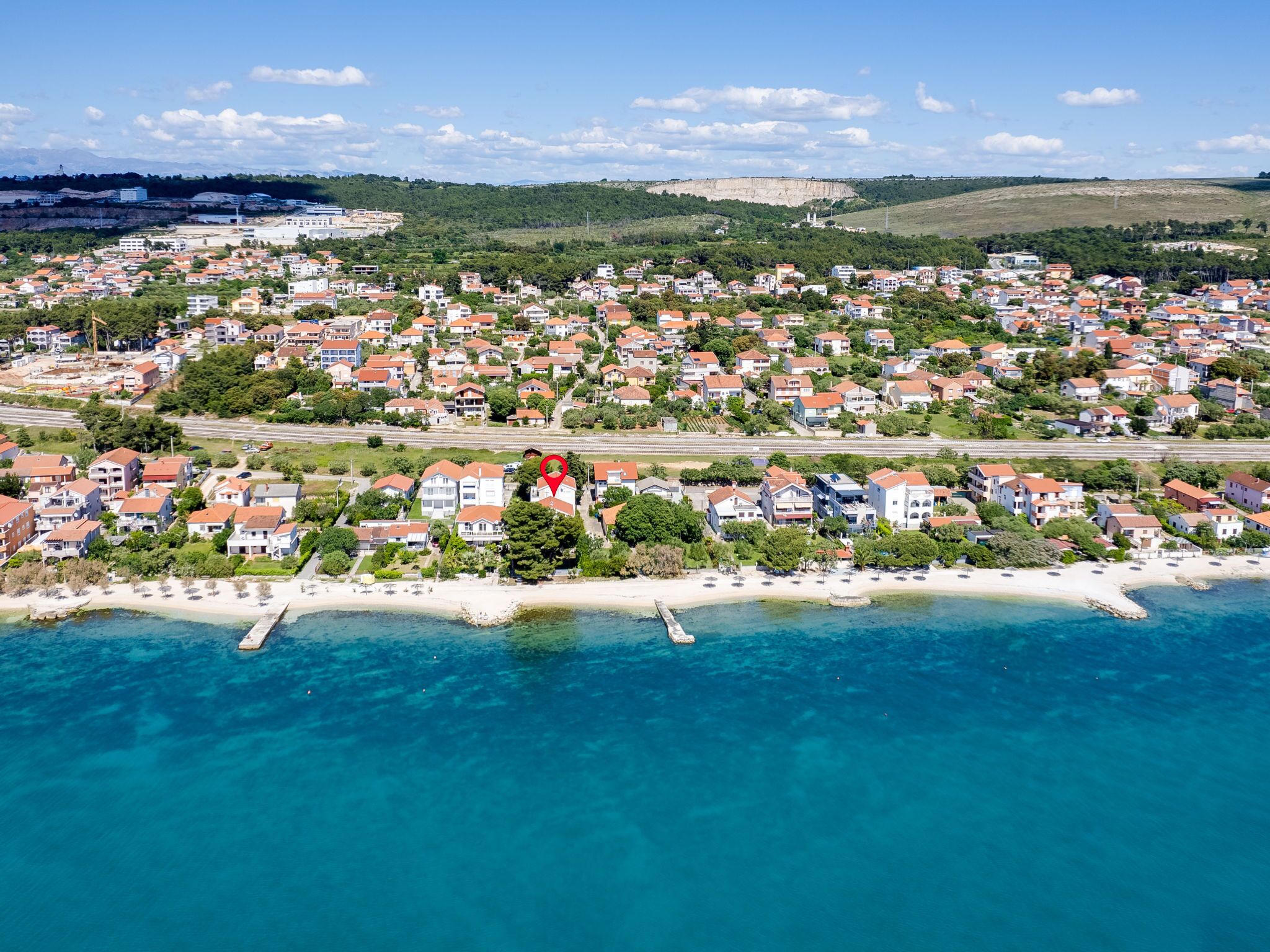 An aerial view of a coastal town with a beach, houses, and a large cliff in the background.