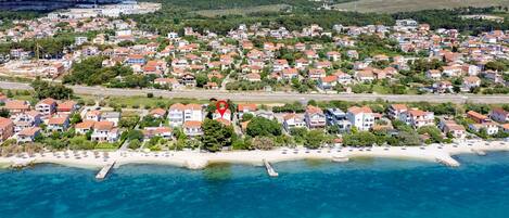 An aerial view of a coastal town with a beach, houses, and a large cliff in the background.