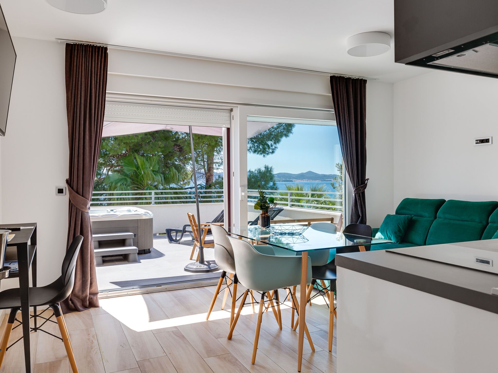 A modern living room with a sofa, a dining area with a table and chairs, and a balcony with a view of the sea and mountains.