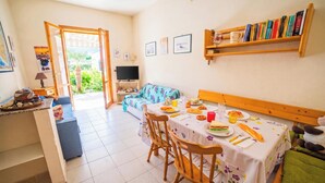 A room with a dining table set for two, a sofa, a TV, and a bookshelf. - Villetta Tesea In Residence Near The Sea, Melendugno, Italy (Melendugno)