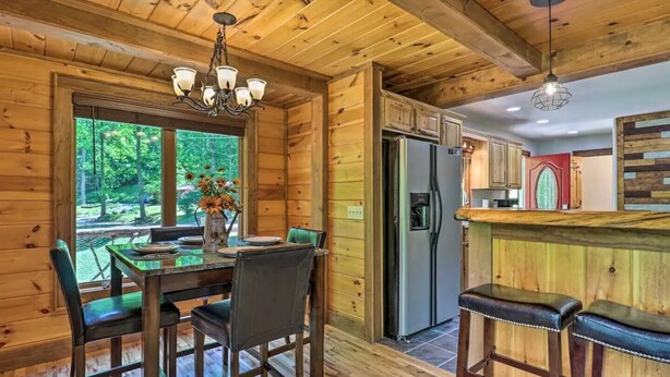 A wooden cabin interior with a dining table, chairs, a refrigerator, and a bar area. - Woodfern Retreat-Pet Friendly EasyCentral Location (Maggie Valley)