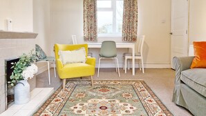 Ein Zimmer mit einem gelben Sessel, einem weißen Schreibtisch, einem gemusterten Teppich und einem grauen Sofa.