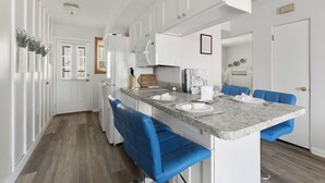 A modern kitchen with white cabinets, a granite countertop, and blue bar stools.