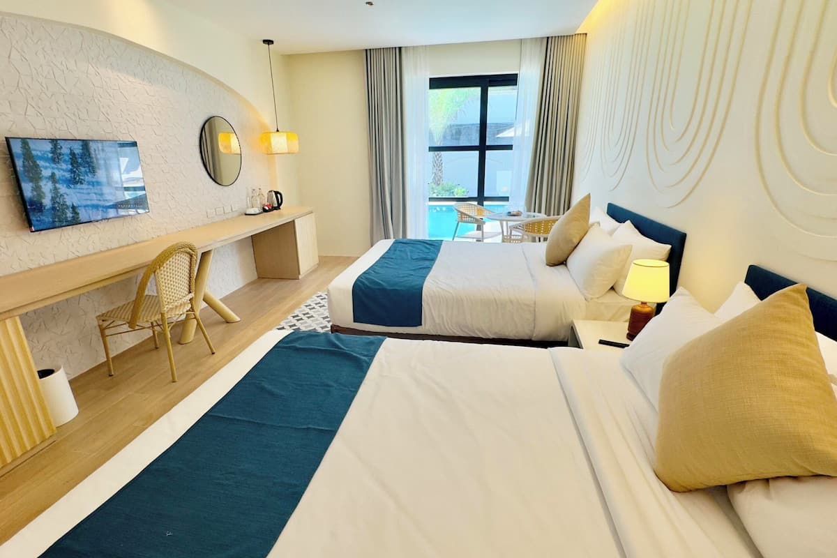 A hotel room with two beds, a desk, a chair, a TV, and a view of the outdoors.