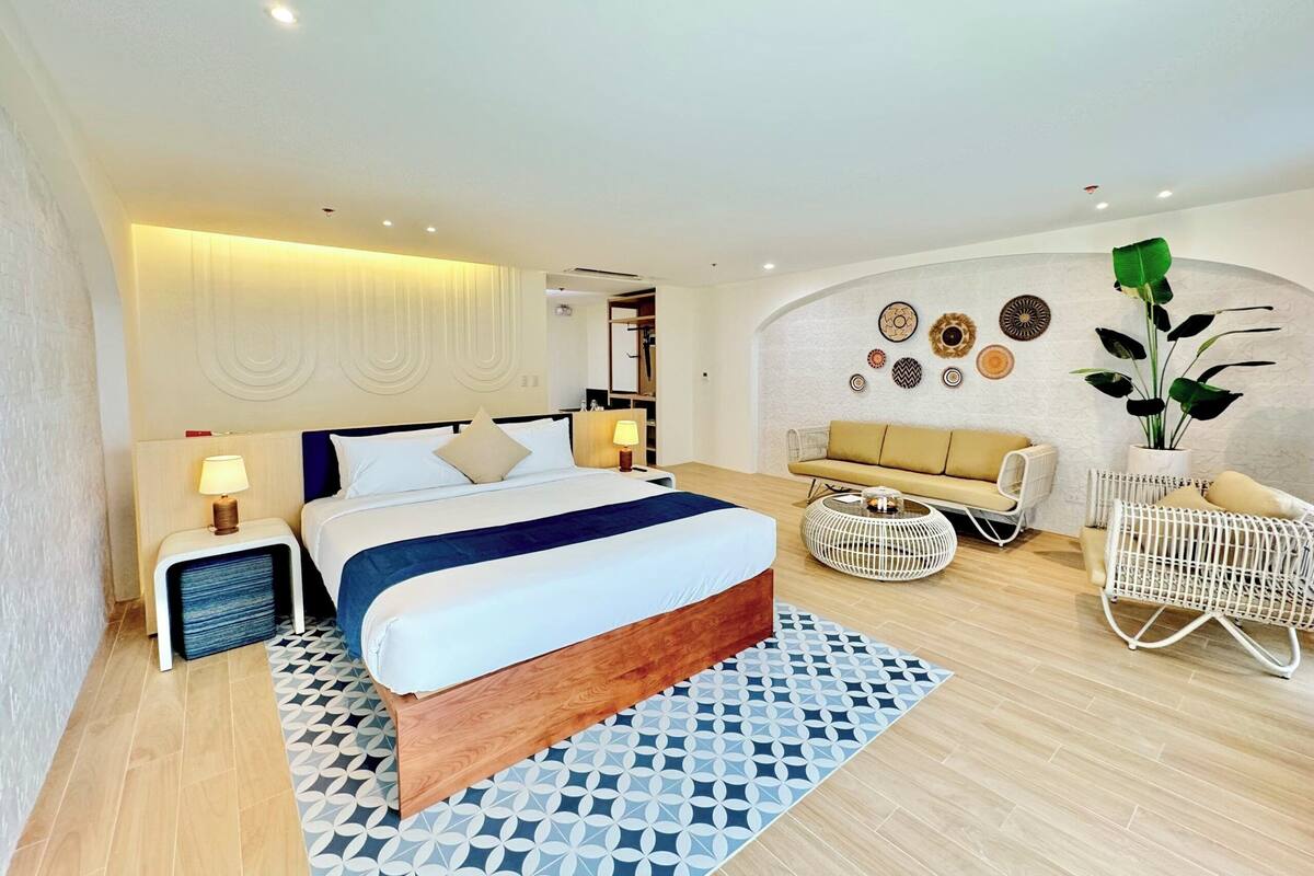 A modern hotel room with a large bed, a sofa, a chair, and a decorative wall.
