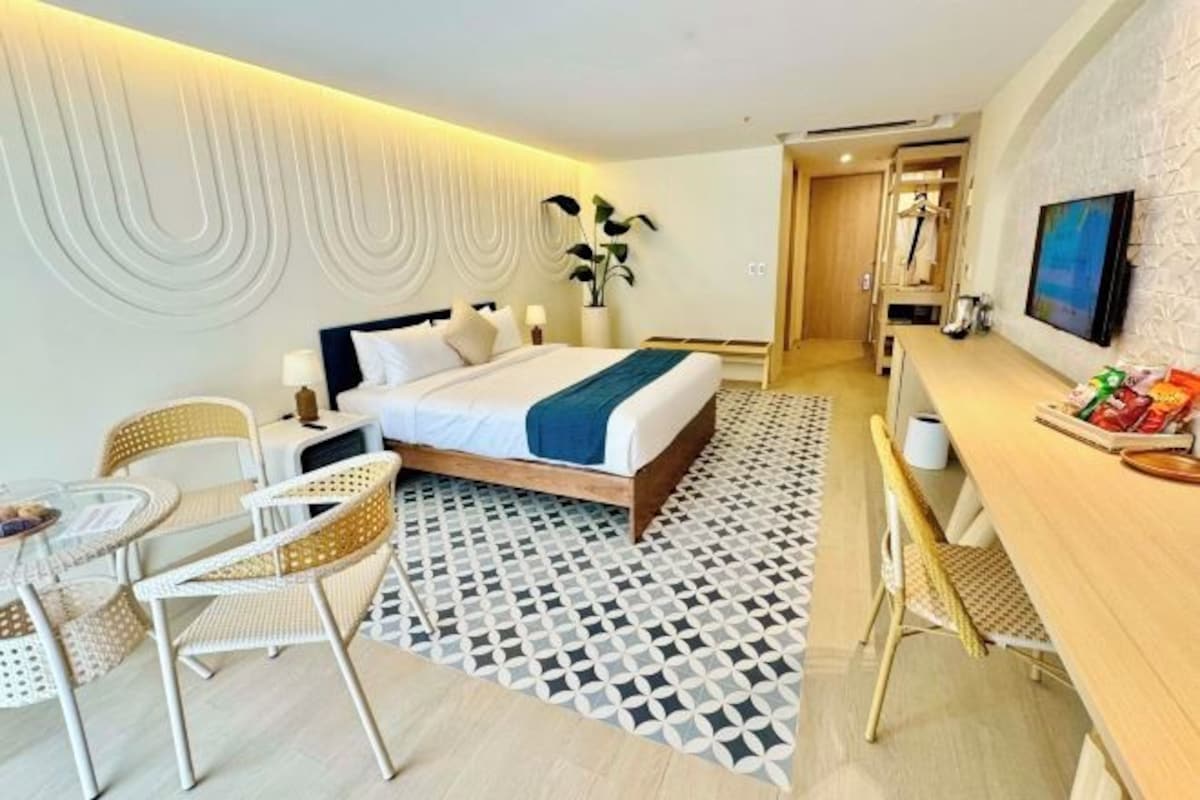A hotel room with a bed, a desk, chairs, a TV, and a bathroom visible through an open door.