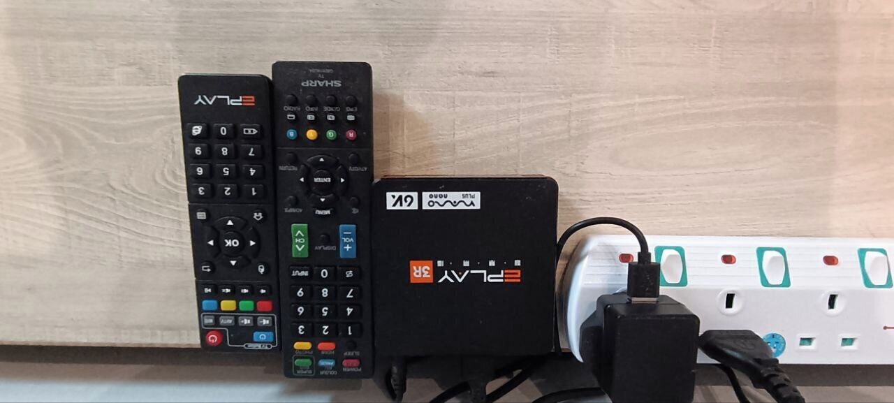 Two remote controls and a power strip on a wooden surface.