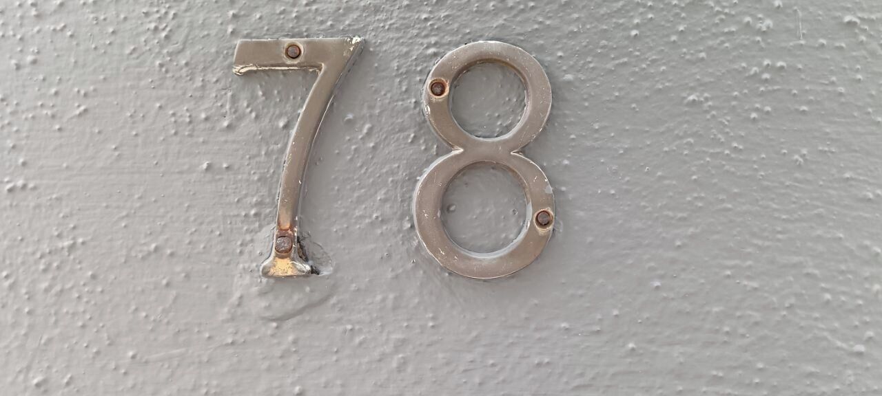 Número 78 de metal fijado en una pared con textura.