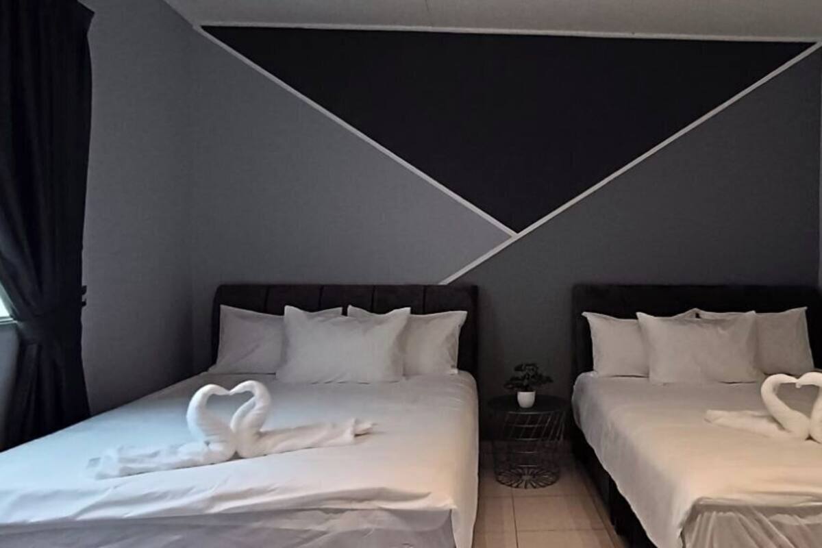 Habitación de hotel con dos camas, cada una con una toalla en forma de corazón, una mesita con una planta y un diseño geométrico en el techo.