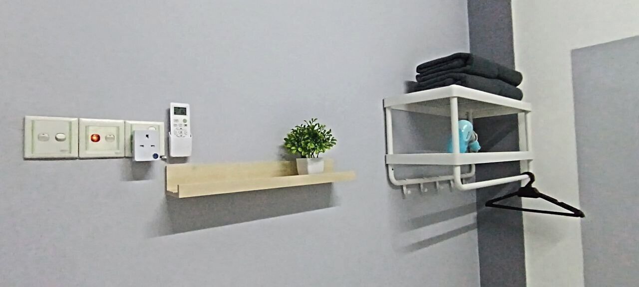 A bathroom with a wall-mounted electrical outlet, a small shelf with a potted plant, and a towel rack with folded towels.