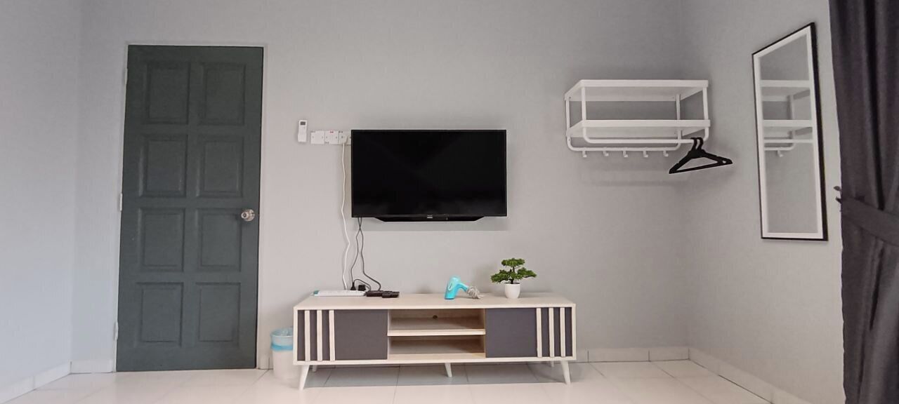 A room with a grey door, a TV mounted on the wall, a white console table with a plant, and a mirror.