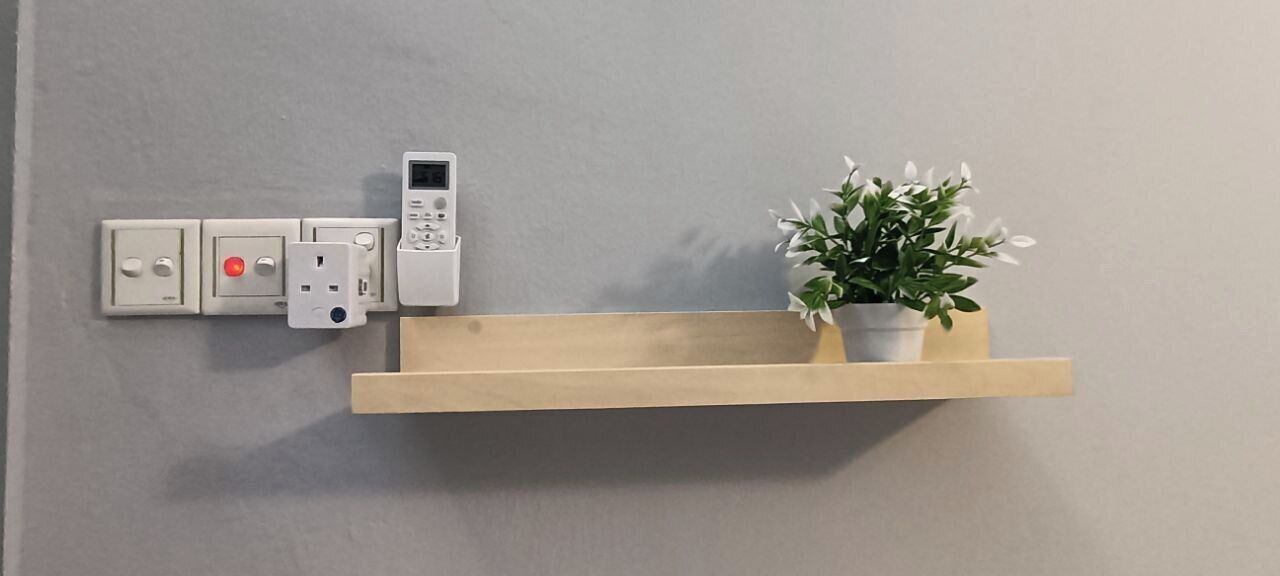 Un panel eléctrico montado en la pared, con un tablero de control y una estantería de madera con una planta en maceta.