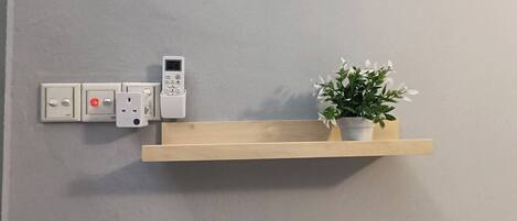 Un panel eléctrico montado en la pared, con un tablero de control y una estantería de madera con una planta en maceta.