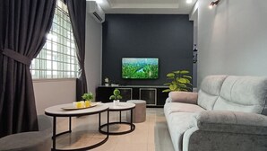 A modern living room with a grey sofa, a small round table, and a flat-screen TV mounted on the wall. - Ipoh Garden East Homestay by Grab A Stay (Ipoh)