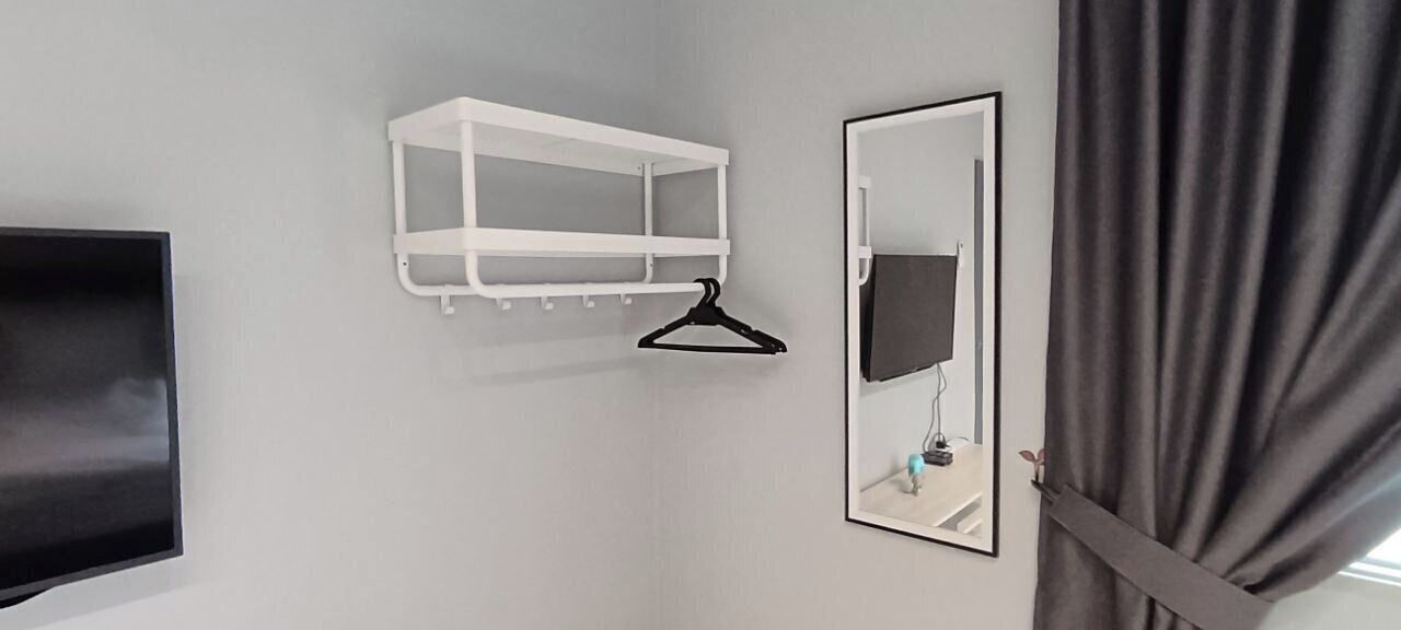 Une pièce avec un téléviseur blanc fixé au mur, une étagère blanche avec un cintre noir et un miroir avec un cadre noir.