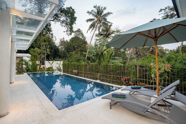A swimming pool with lounge chairs and an umbrella, surrounded by lush greenery and palm trees. - AR Villa Sayan (Ubud)