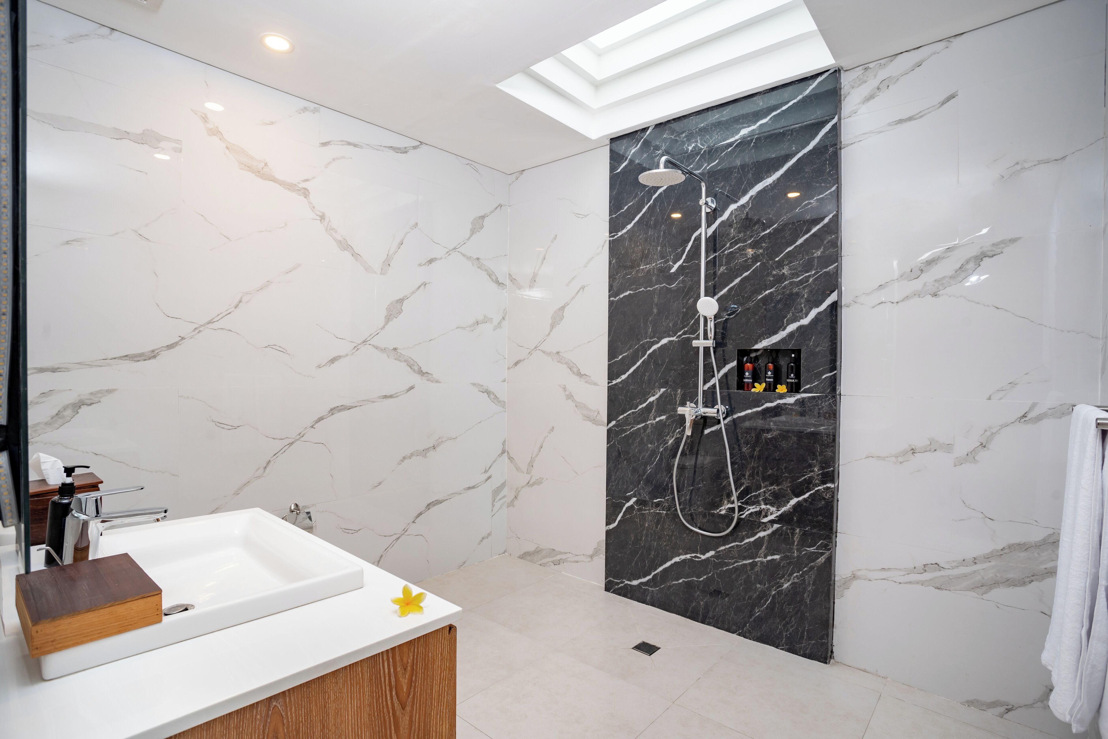 Une salle de bain moderne avec un meuble-lavabo en marbre blanc, une douche avec un mur en marbre noir et une lucarne au-dessus.