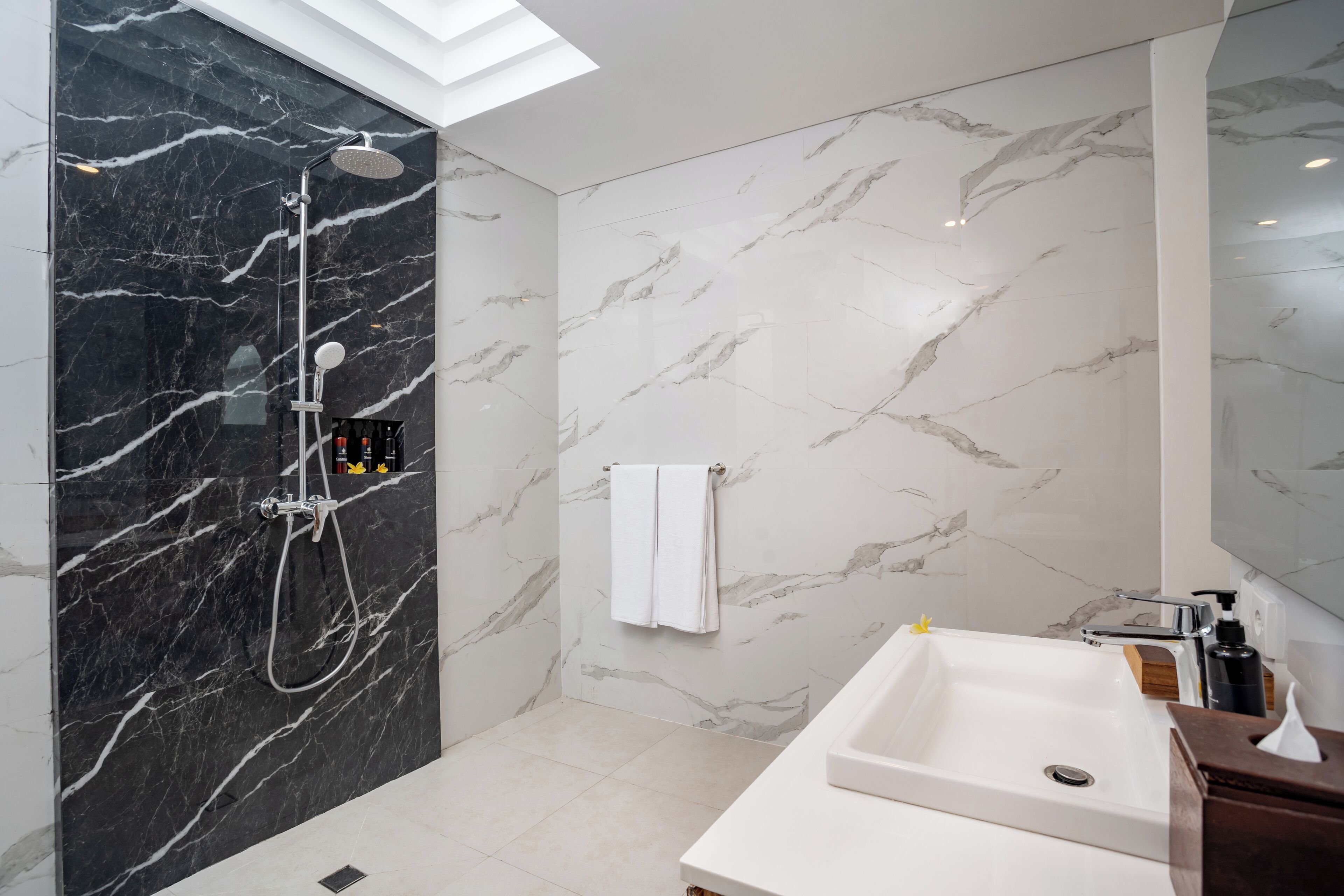 Un bagno moderno con doccia in marmo nero e bianco, lavandino bianco e mobile contenitore in legno.
